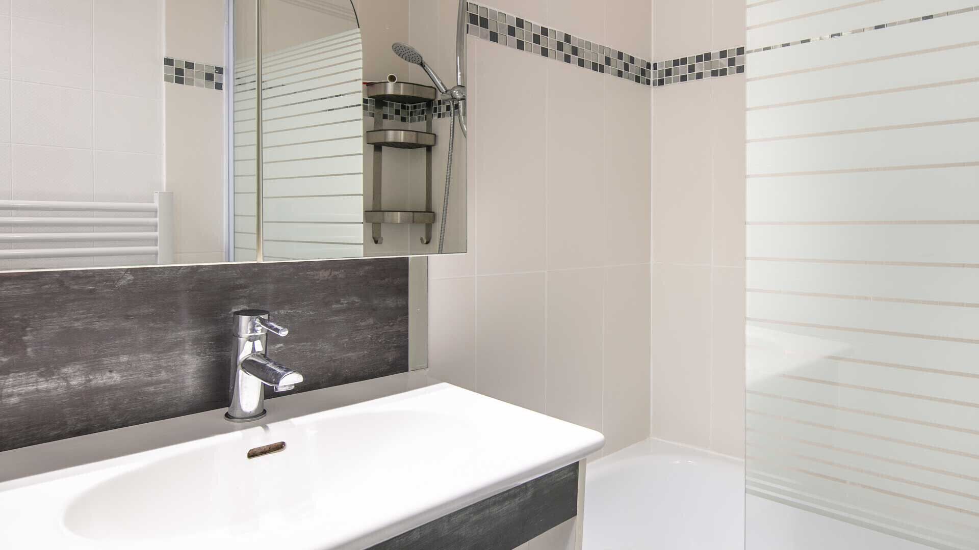 A modern bathroom with a white sink, a mirror, and a shower area.