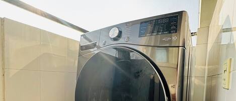 A compact, modern washing machine in a small, tiled laundry room with a slanted ceiling.