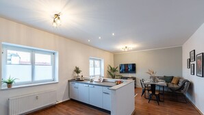 Eine moderne Küche mit weißen Schränken, einem Essbereich mit Tisch und Stühlen sowie einem an der Wand montierten Fernseher.