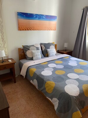 Un dormitorio ordenado con una cama, una mesita de noche, una lámpara y un cuadro en la pared.