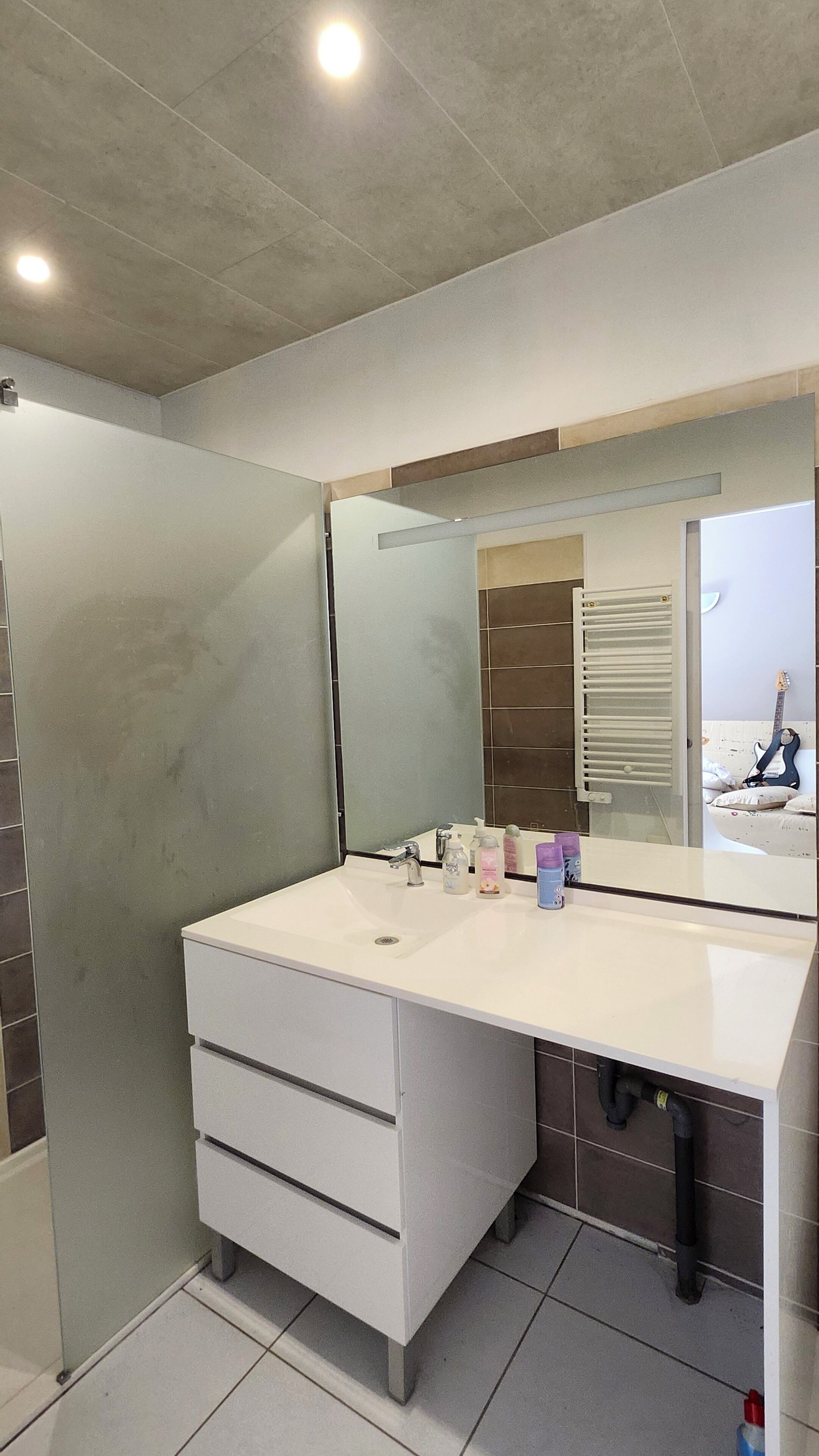 Een moderne badkamer met een grote spiegel, een witte wastafel en een betegelde vloer.
