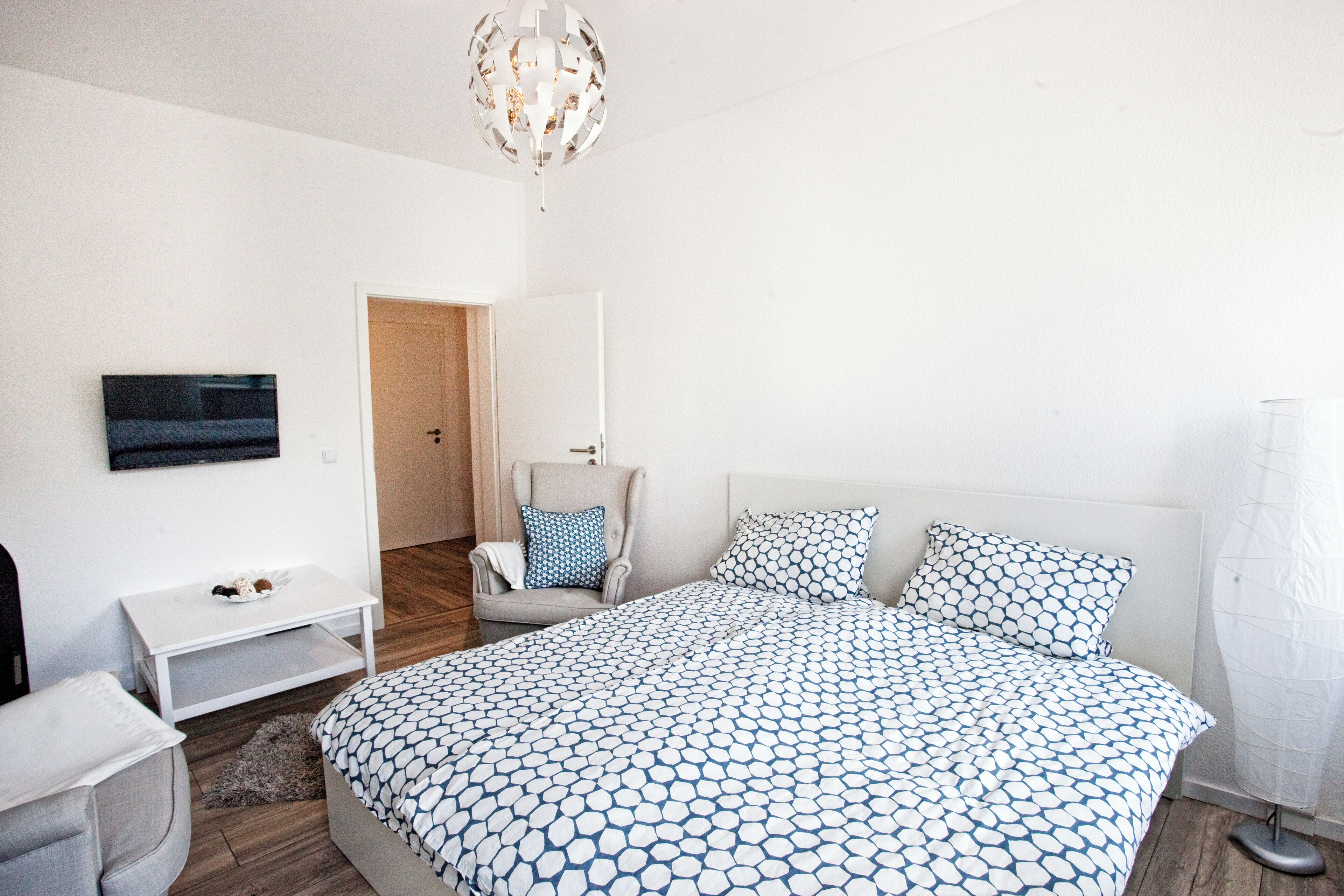 Un dormitorio con cama, una silla, un televisor y una puerta.