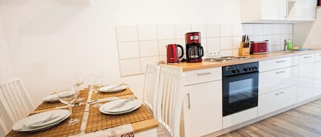Une cuisine moderne avec des meubles blancs, un plan de travail en bois et une table à manger pour quatre personnes.
