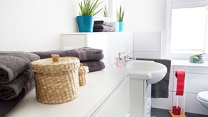 Ein Badezimmer mit einem weißen Waschbecken, einem Spiegel, einem Handtuchhalter mit Handtüchern und zwei Blumentöpfen auf einem Regal.