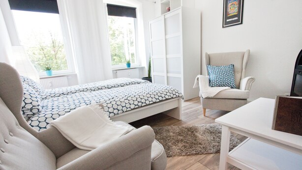 Ein modernes Schlafzimmer mit einem Bett, einer Couch, einem Sessel und einem Fernseher.