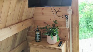 A wooden interior with a mounted flat-screen TV, a small table with a potted plant, a decorative metal container, and a power outlet.