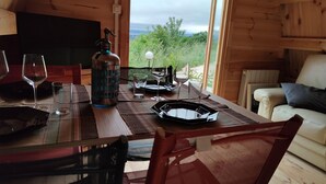 A wooden cabin with a dining table set for two, a sofa, and a view of the outdoors.