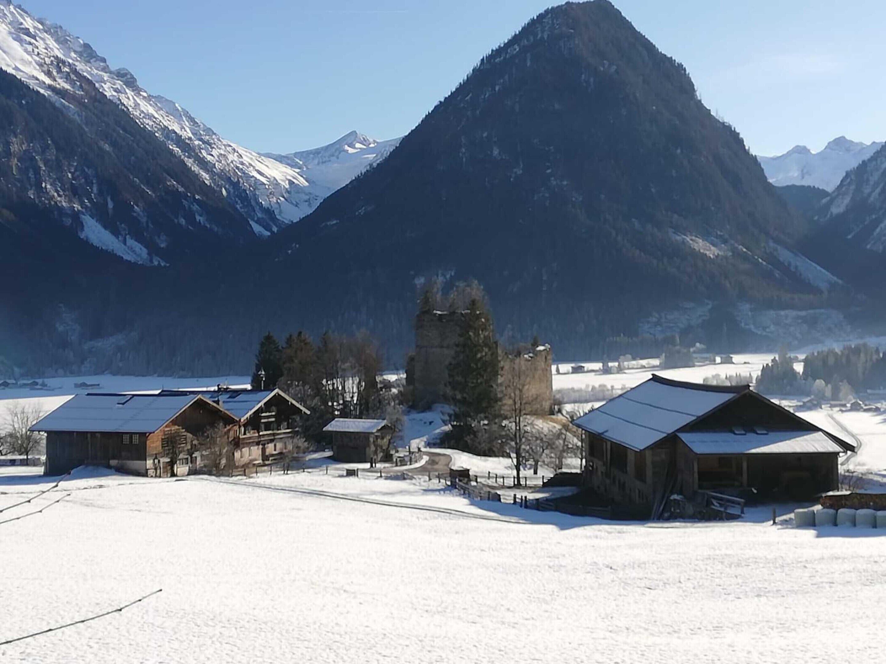 A rural village with wooden buildings, a snow-covered landscape, and mountains in the background.