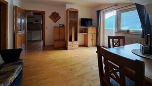 Habitació amb terra de fusta, taula de dinar amb cadires, televisió sobre un moble de fusta i finestra amb cortines.