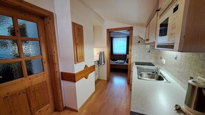 Passadís estret amb terres de fusta, zona de cuina amb rentapeus i armaris, i finestra amb vista a l'exterior.