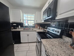 A modern kitchen with white cabinets, a black refrigerator, a stainless steel stove, and a window providing natural light. -  Welcome to Casa Alafia at Riverview. (Riverview)