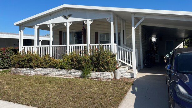 A two-story house with a covered porch, a stone retaining wall, and a parked car.