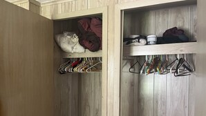 A wooden closet with shelves and hanging space, containing folded clothes and hangers.