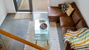 A modern living room with a glass coffee table, a brown leather sofa, and a view through a glass door to a wooden deck. - 2BR Loft |A/C, Netflix, Private Deck| Walk to City (Auckland Central)