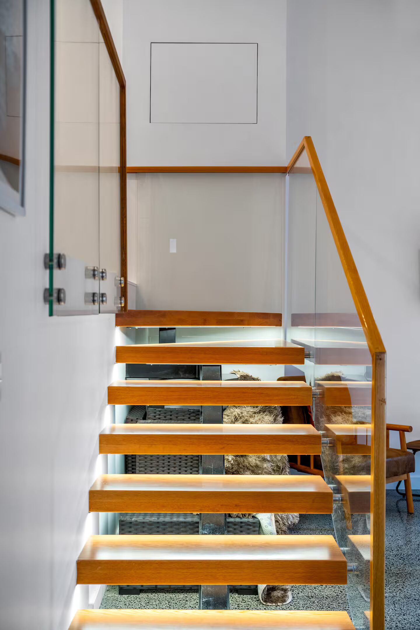A modern staircase with wooden steps and glass railings, leading to a room with a white door and a framed picture on the wall.