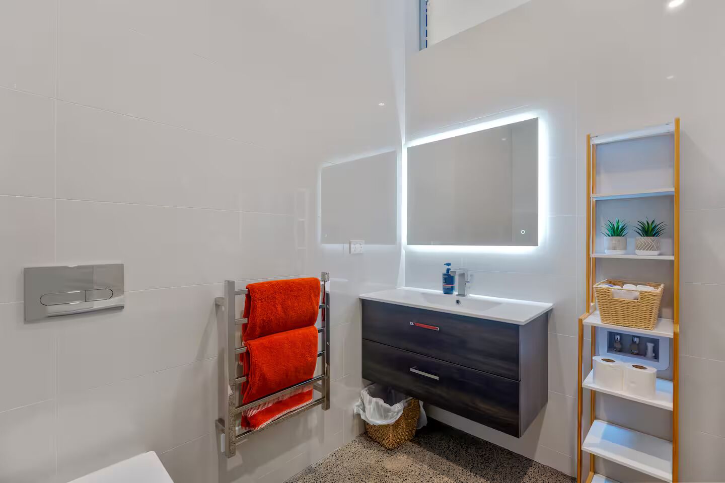 Een moderne badkamer met een witte betegelde muur, een handdoekhouder met twee rode handdoeken, een wastafel met spiegel en een plank met toiletartikelen.