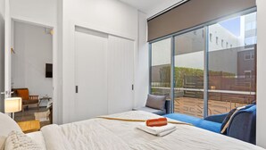 A hotel room with a large bed, a sofa, a TV, and a balcony with a view of the outside. - 2BR Loft |A/C, Netflix, Private Deck| Walk to City (Auckland Central)