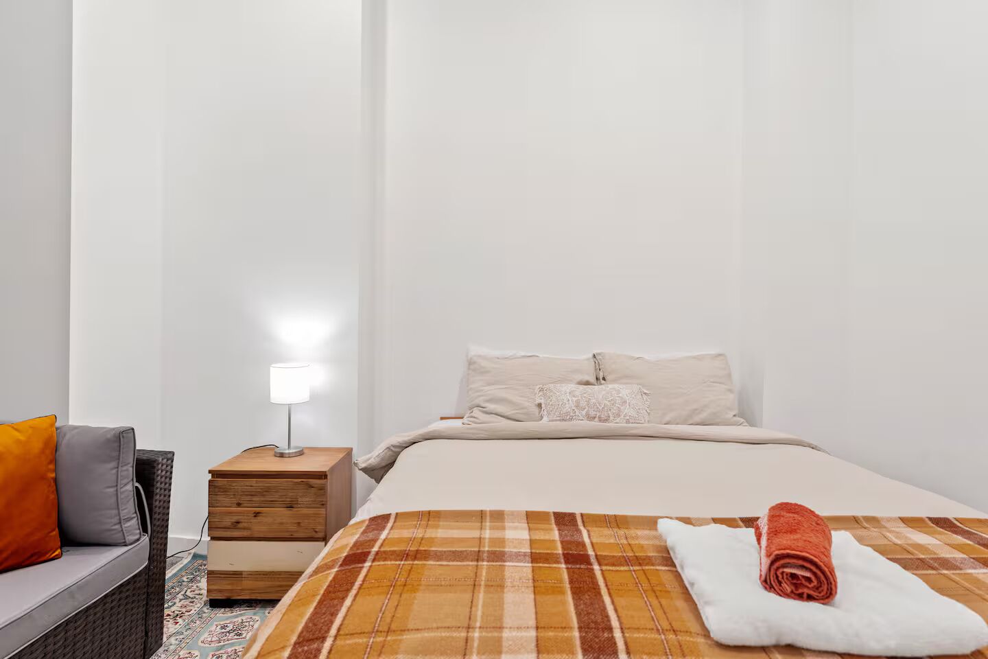 Een slaapkamer met een bed, nachtkastje, lamp, bank en een kamerbreed tapijt met dessin.