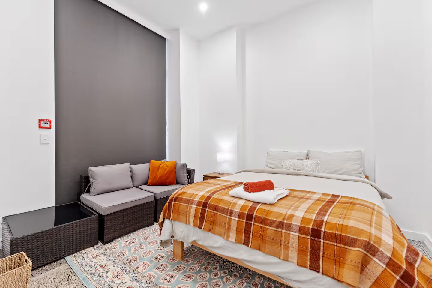 A modern hotel room with a bed, a sofa, a small table, and a patterned rug.