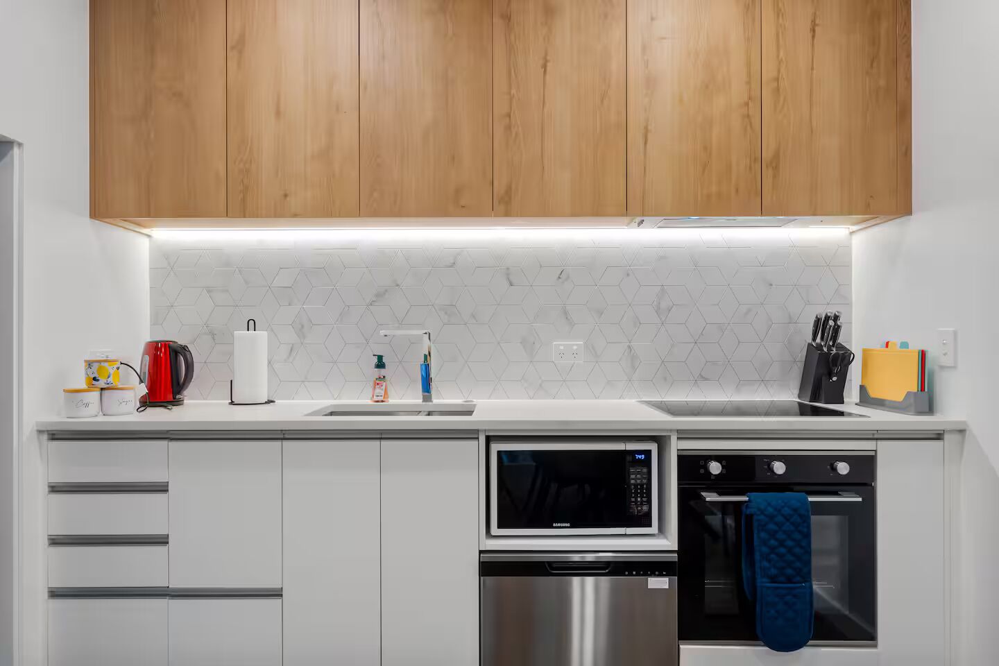 A modern kitchen with white cabinets, a microwave, an oven, and a sink.