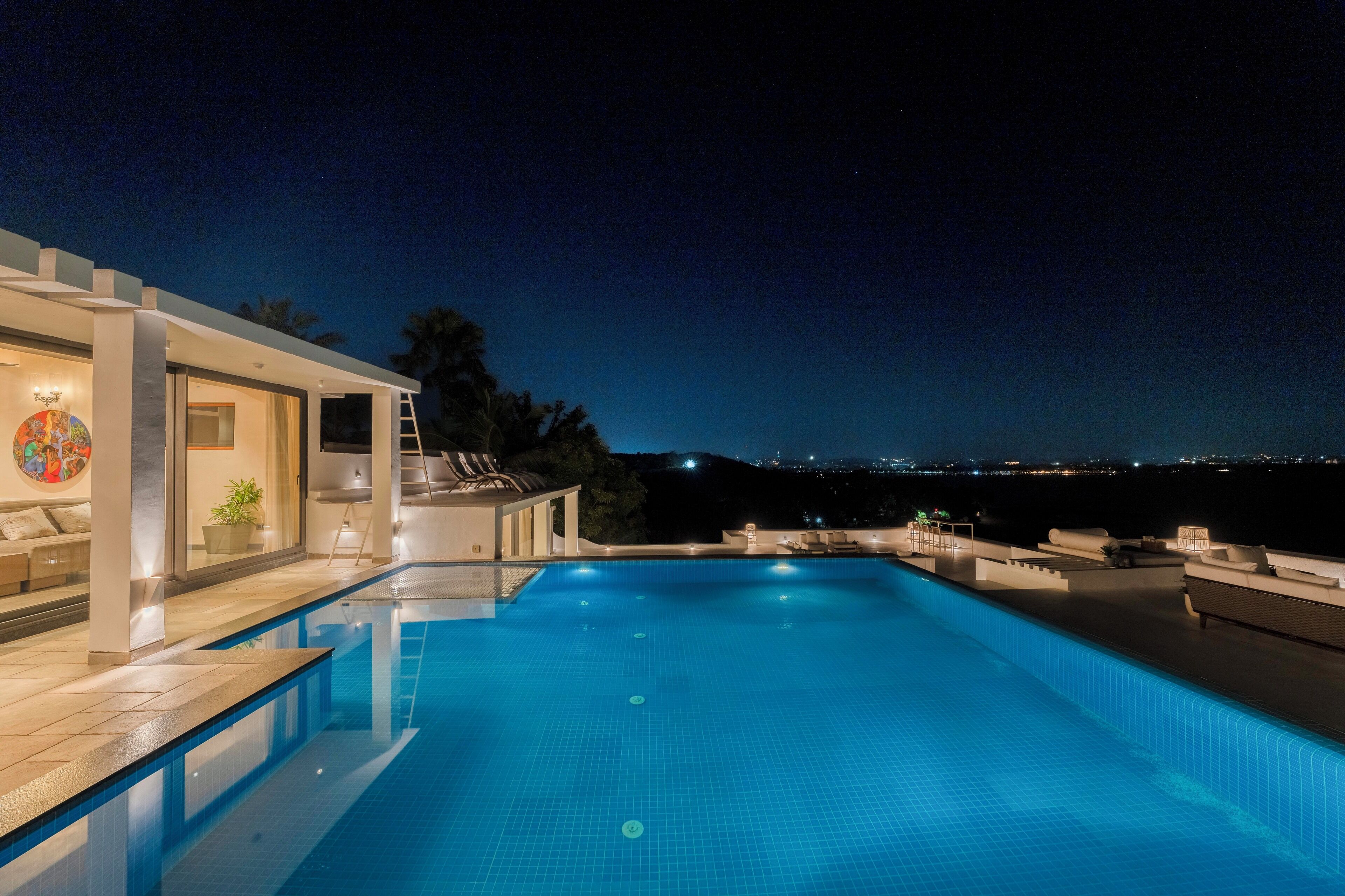 Une piscine à débordement moderne offrant une vue dégagée sur les gratte-ciel de la ville la nuit.