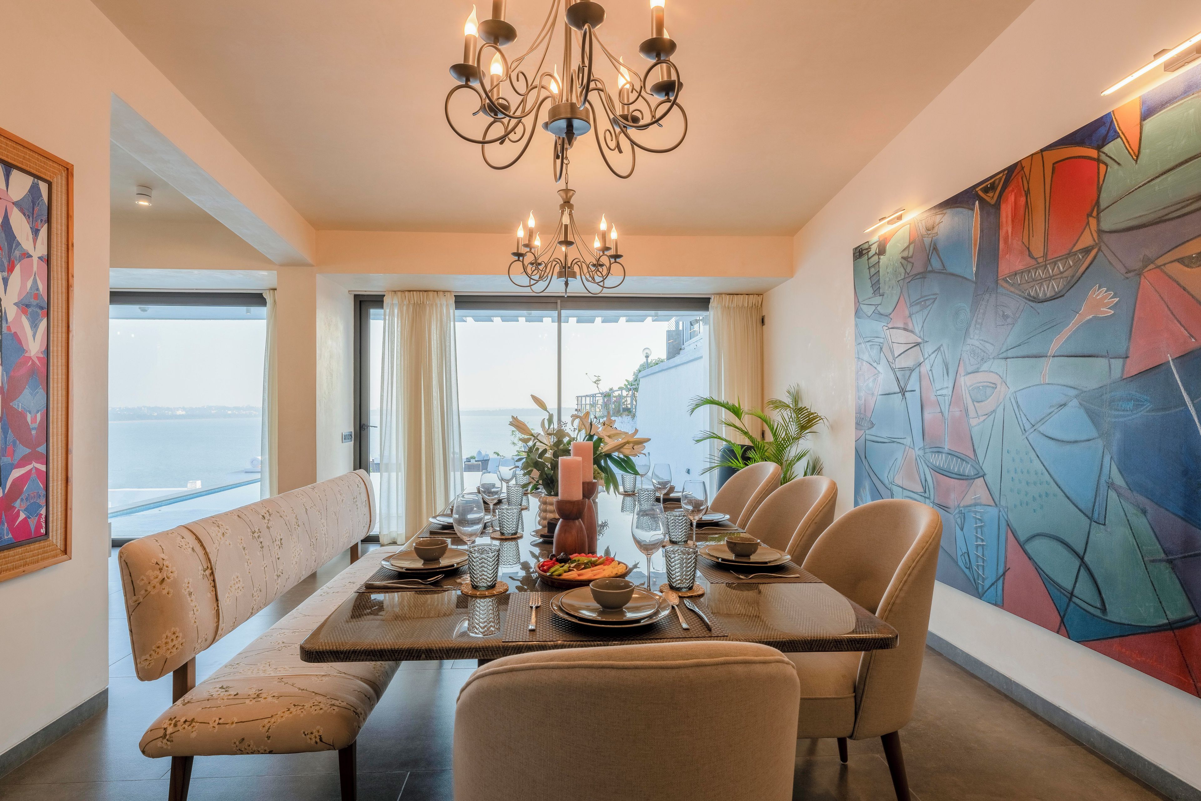 Un comedor con una araña, una mesa dispuesta para seis comensales y vista al mar.