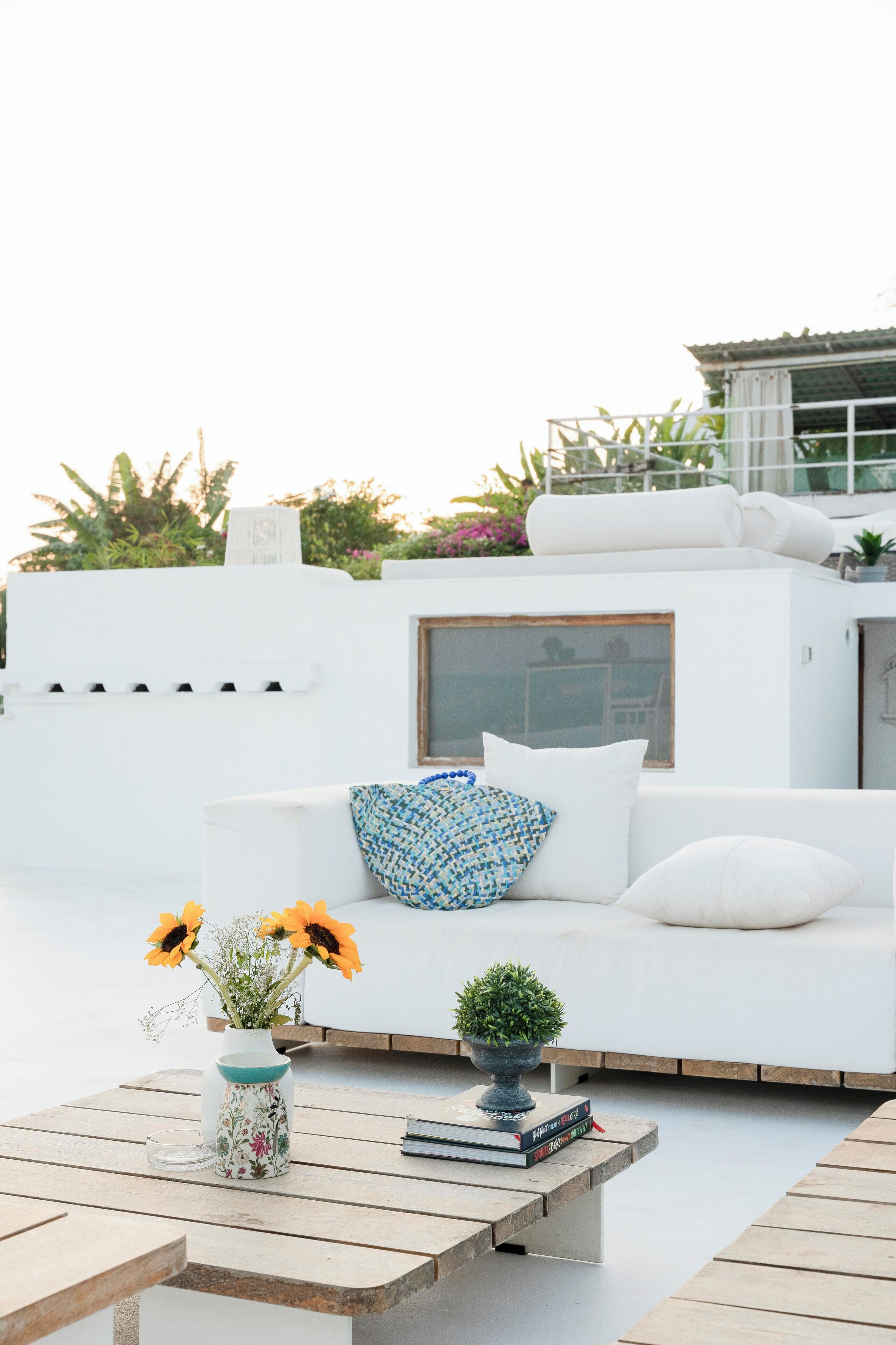 A white outdoor seating area with a sofa, a coffee table, and a vase with sunflowers.