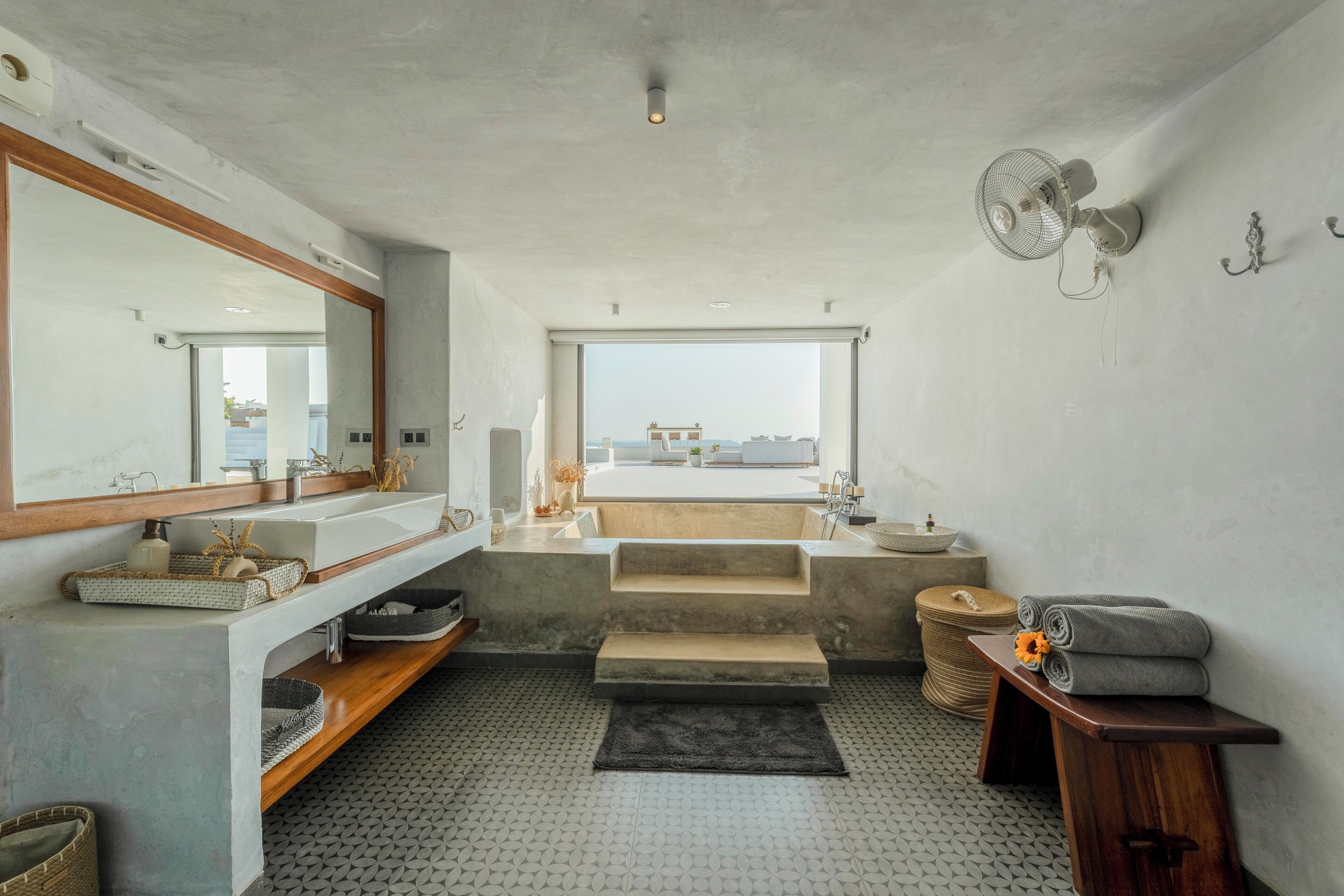 A modern bathroom with a large mirror, dual sinks, a freestanding bathtub, and a ceiling fan.