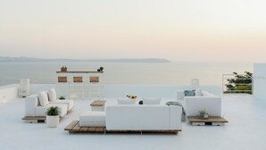 Eine Dachterrasse mit weißen Möbeln, einem Tisch und Stühlen mit Blick auf ein Gewässer.