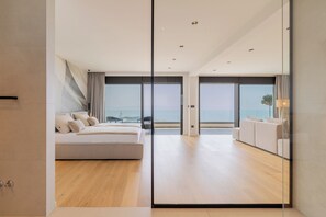 A modern bedroom with a large bed, a sofa, and a view of the ocean. - Villa Reina (Makarska)