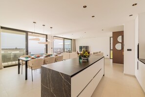 A modern kitchen with a marble island, a dining area with a glass table, and a view of the sea. - Villa Reina (Makarska)
