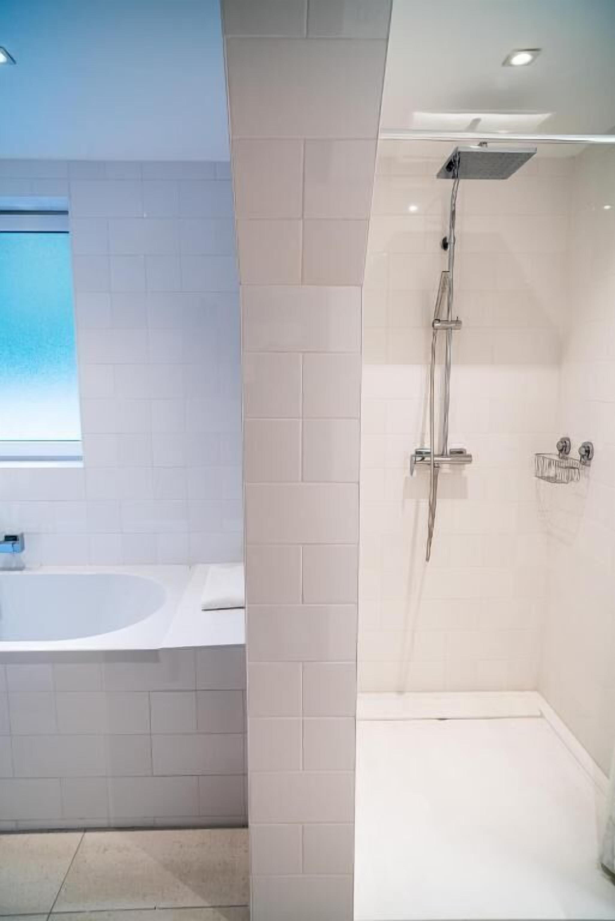 A modern bathroom with a freestanding bathtub, a glass-enclosed shower, and a window providing natural light.