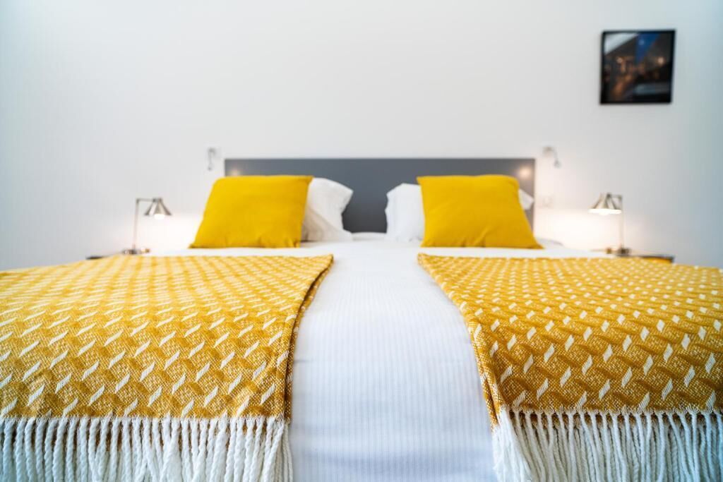 A double bed with two pillows, a white bedspread, and two matching throw blankets with fringe.