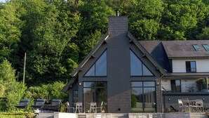 Une maison moderne dotée d’une cheminée imposante, de grandes fenêtres et d’une façade en pierre.
