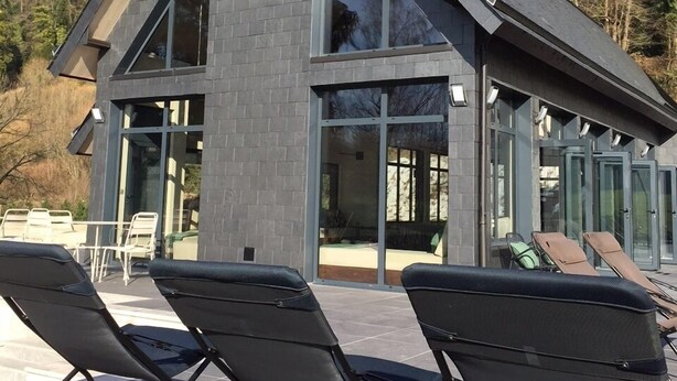 Une maison moderne avec un toit en pente, de grandes fenêtres et une terrasse dotée de chaises longues.