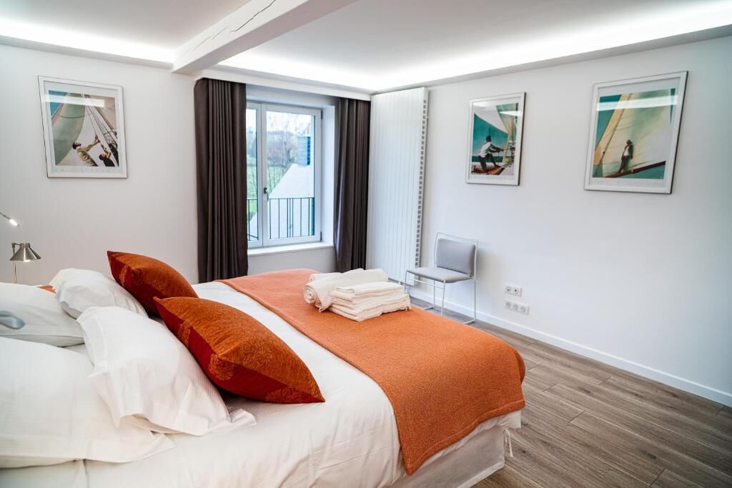 Ett modernt hotellrum med en stor säng, ett fönster med gardiner, en stol och konstverk på väggarna.