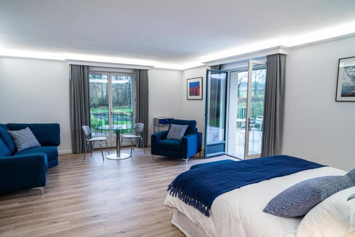 A modern hotel room with a bed, a blue sofa, a chair, and a balcony with a view.