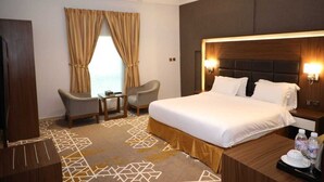 A hotel room with a large bed, two armchairs, a small table, and a nightstand with a lamp. - Taj Al- Wajh hotel   (Al Wajh)