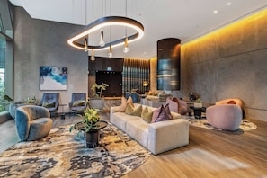 A modern lobby with a sofa, chairs, a rug, and a large plant. - Designer CBD Suite. Gym, Heated Pool, Sauna, Steam, Opposite Southern Cross (Melbourne)