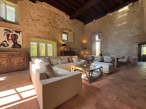Un salon spacieux avec un mur en pierre, un grand canapé, une table basse et un coin repas avec des chaises.
