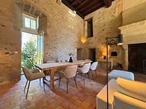 A rustic dining area with a wooden table and chairs, a fireplace, and a stone wall.