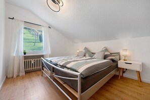 A bedroom with a metal bed frame, a bedside table with a lamp, a window with curtains, and a radiator.