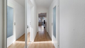 A hallway with white walls and wooden flooring, leading to a room with a large window. - Apartment 'Kraft' with Mountain View, Balcony and Wi-Fi (Bad Wildbad)