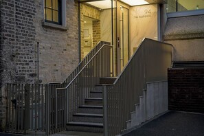 A staircase leading to a building entrance with a number '94' sign, a brick wall, and a metal railing.