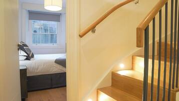 A staircase with wooden steps and black railings, leading to a bedroom with a bed and a window.