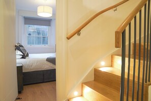 Una escalera de madera con barandas negras que conduce a un dormitorio con cama y ventana.