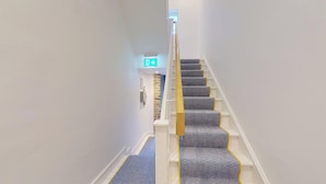 Un escalier recouvert d’une moquette à motifs et muni d’une main courante, menant à un panneau indiquant la sortie sur le mur.