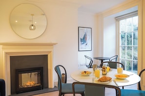 A dining area with a fireplace, round table, chairs, and breakfast items.