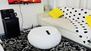 A modern living room with a flat-screen TV mounted on the wall, a black coffee machine, a white sofa with yellow and black polka dot cushions, and a round ottoman. - Quantity studio in Ngara, 3mins drive to Nairobi Cbd (Nairobi)