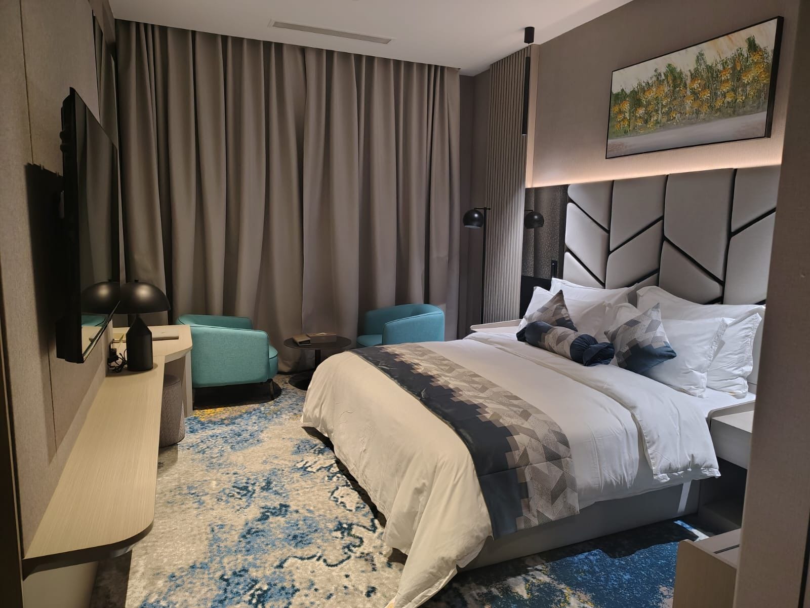 Una habitación de hotel moderna con una cama grande, un escritorio, una silla y un cuadro en la pared.